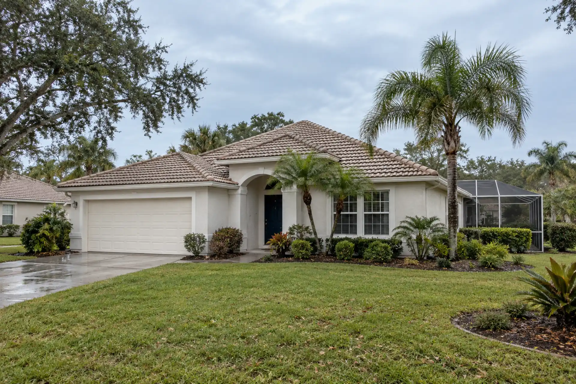 A pale stucco home with a tile roof and screened enclosure.