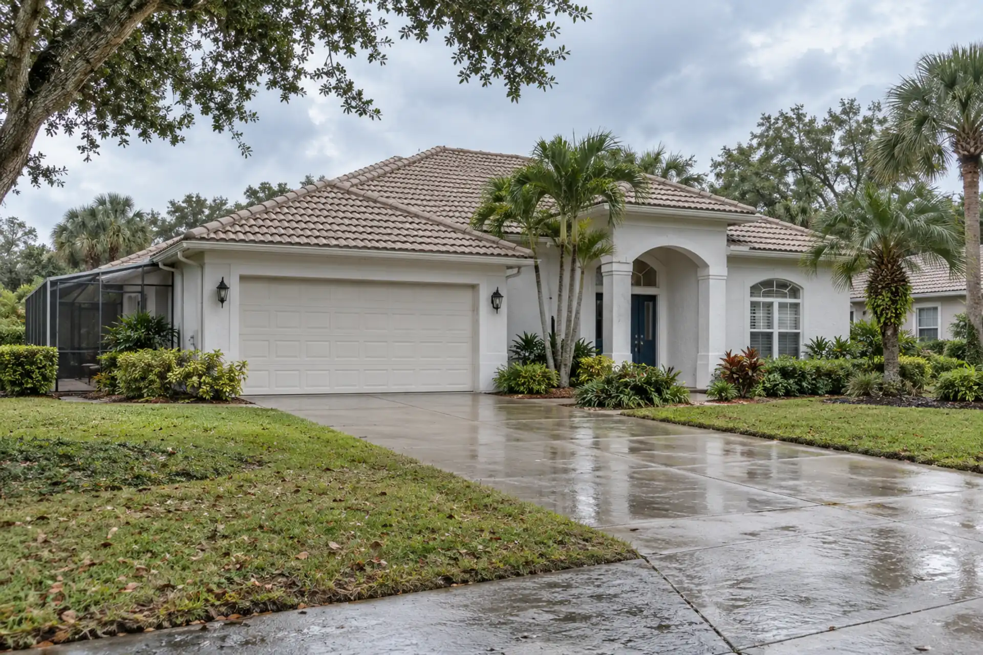 A stucco home with a tile roof and a screened patio beside palms.