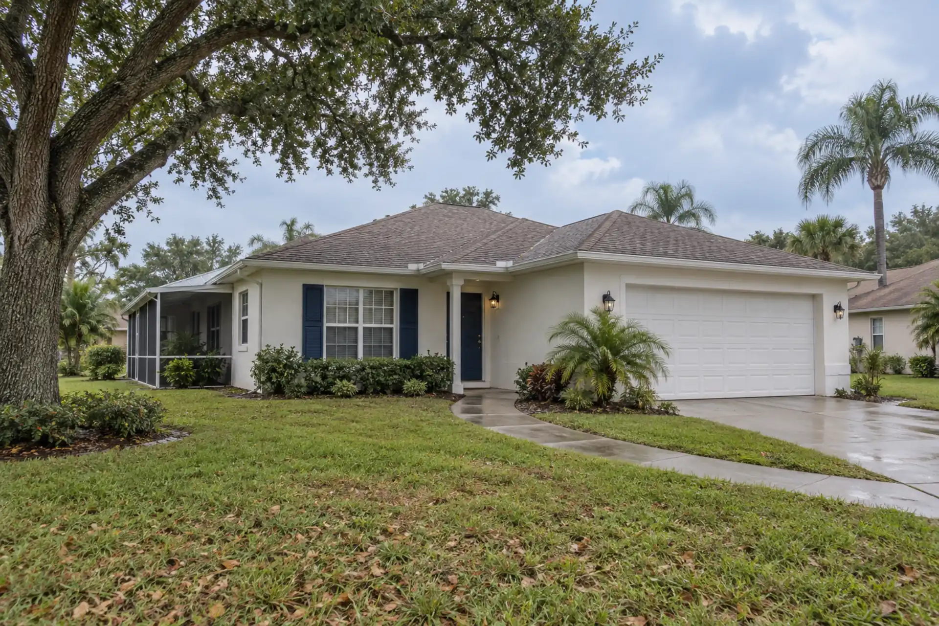 A stucco home with a shingle roof, live oak and damp walkway.