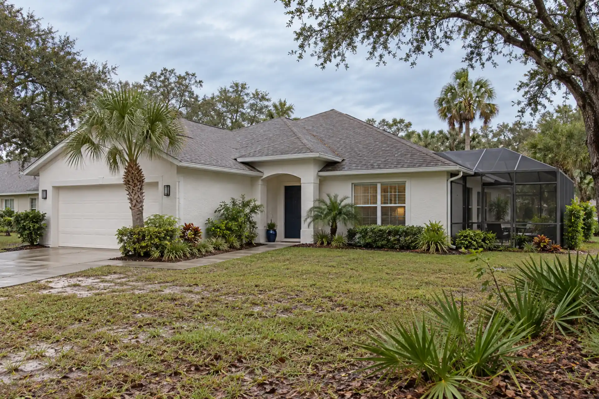 A stucco ranch beside scrub oaks, palms and a sandy lawn.